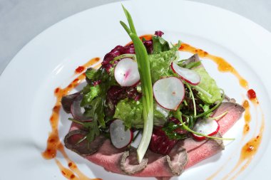 Güzel dekore edilmiş salata dili, beyaz tabakta sebze ve sos.