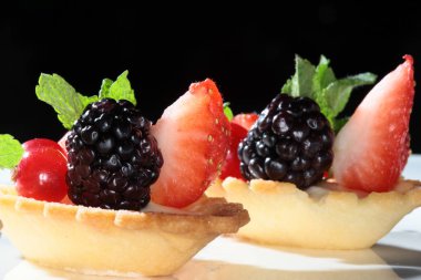 Koyu bir arka plan stüdyosunda çilek ve böğürtlenli lezzetli bir pasta.