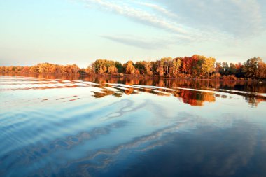 Sonbahar manzarası nehirde güzel bir sabah kumsalda renkli ağaçlar ve mavi gökyüzünde bulutlar.