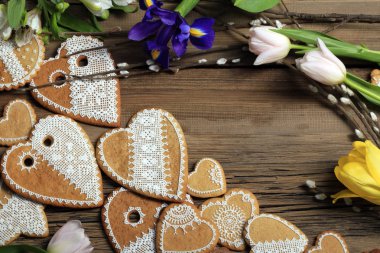  Sarı kurdeleli kalp şeklinde makro zencefilli kurabiye, ahşap arka planda çiçekler.