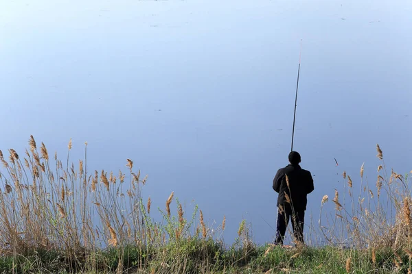 春の朝の穏やかな川の岸に釣り竿を持つ漁師 — ストック写真