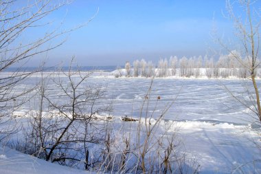 Buz deposunun altındaki manzaralı kış manzarası. Muhteşem mavi gökyüzü sisi ve kıyı şeridindeki ağaçlarda don.