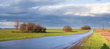 İlkbahar yağmurlu yolları ufka götürür yeşil tarlalar ve bulutlu gökyüzü arasında