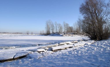 Kış manzarası nehri açık mavi gökyüzü ve güneşli bir öğleden sonra sahilde ağaçlar.