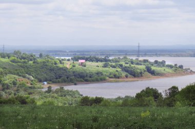 Geniş bir nehrin yaz manzarası ve bulutlu bir günde sahilde ağaçlar.