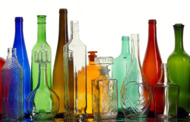 Beyaz ışık stüdyosundaki ayna yüzeyinde farklı şekillerde şeffaf renkli cam şişeler var.