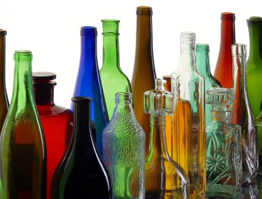 Beyaz ışık stüdyosundaki ayna yüzeyinde farklı şekillerde şeffaf renkli cam şişeler var.