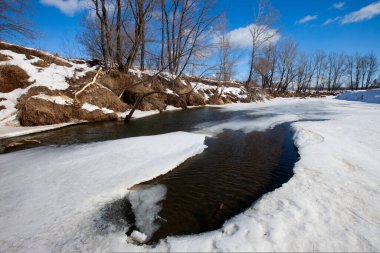 İlkbaharın başlarında harika bir manzara nehirde ve güneşli bir günde mavi gökyüzünde beyaz bulutlar