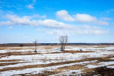 Geniş tarlalarda kar eriyor ilkbaharın başlarında, bulutlu bir günde gün batımında.