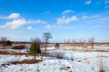 Geniş tarlalarda kar eriyor ilkbaharın başlarında, bulutlu bir günde gün batımında.