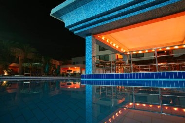 Yazın deniz kenarı otel binası ve havuzlu peyzaj alanları.