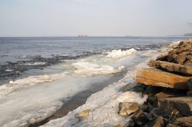 Nehir manzarası diseksiyonu ve ilkbaharın başlarında buz sürüklenmesi, kıyıdaki yapraksız ağaçlar ve bulutlu gökyüzü