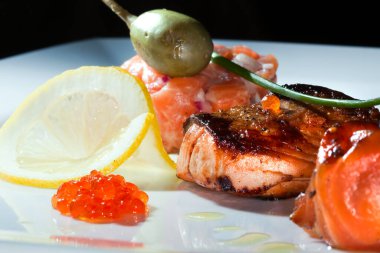 Kızarmış balık, havyar, limon, koyu arkaplanda kiraz domatesleri ve kapari stüdyolarıyla süslenmiş makro lezzetli bir yemek.