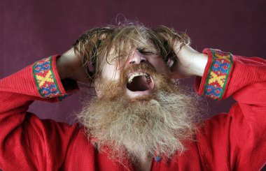 Kırmızı gömlek stüdyosunda uzun sakallı, bıyıklı ve ıslak sarı saçlı kutsanmış birinin yakın plan portresi.