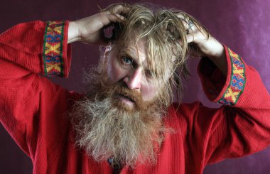 Kırmızı gömlek stüdyosunda uzun sakallı, bıyıklı ve ıslak sarı saçlı kutsanmış birinin yakın plan portresi.