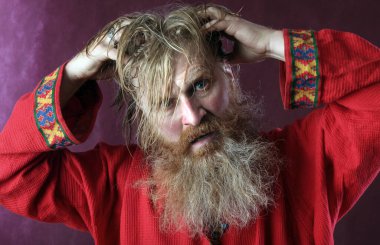 Kırmızı gömlek stüdyosunda uzun sakallı, bıyıklı ve ıslak sarı saçlı kutsanmış birinin yakın plan portresi.