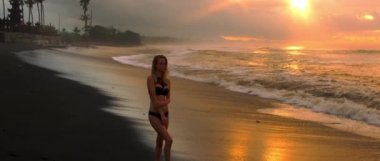 Okyanus ve geniş açılı genç bir kadınla siyah kumsalda serin kırmızı gün doğumu.