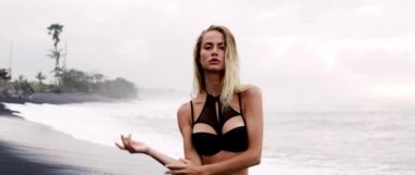 Okyanus dalgaları ve genç kadın portresiyle siyah kumsalda gün doğumu.