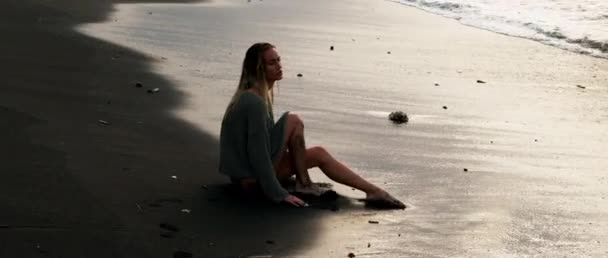 Joven Chica Piel Bronceada Sentada Playa Arena Negra Profunda Mira — Vídeo de stock