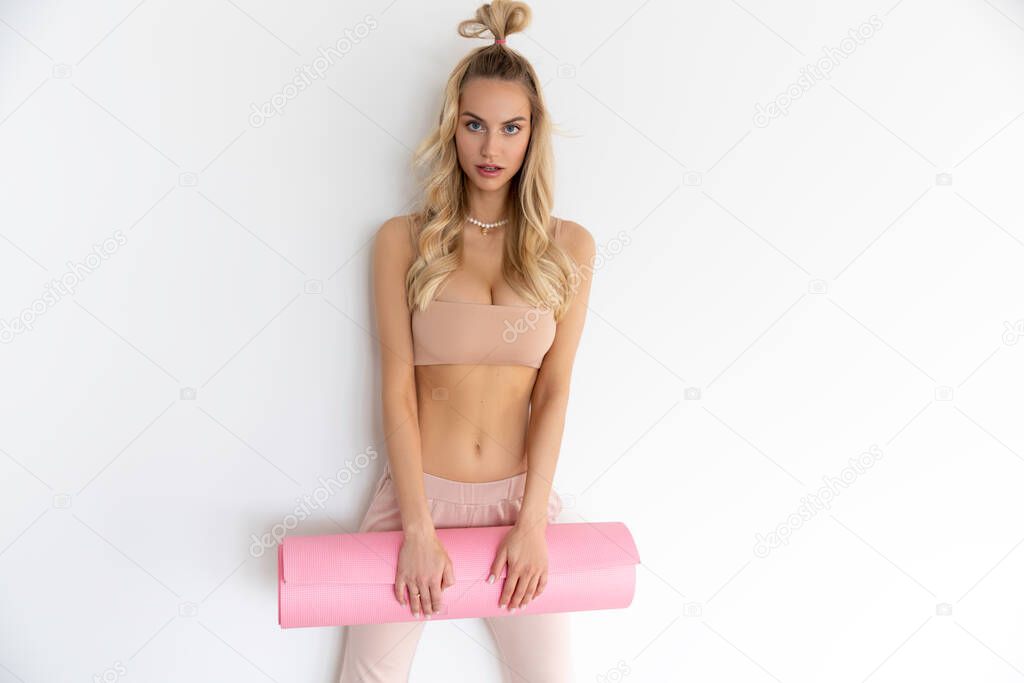 Skinny sporty blonde Girl in sportwear posing with pink mat