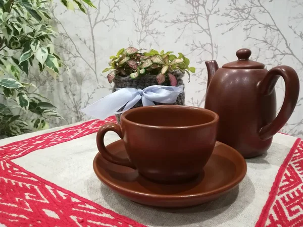 Çay fincanı, krema ve fındık ezmesi örülmüş bir tencerede keten işlemeli peçete arka planında.