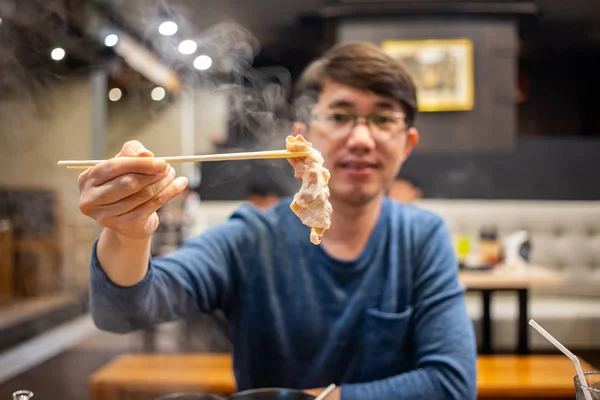 Japon Shabu restoranında elinde bambu çubukları ve bir parça haşlanmış et tutan bir adam.
