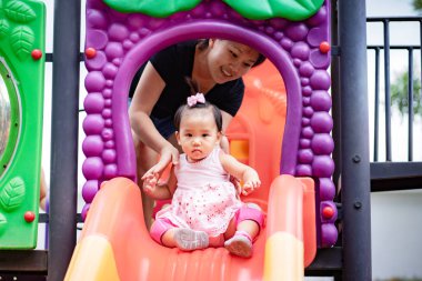 Bebek kız ilk kez parkta sürgülü oynuyordu, annesi kızına sürgülü kayıkta bakıyordu.