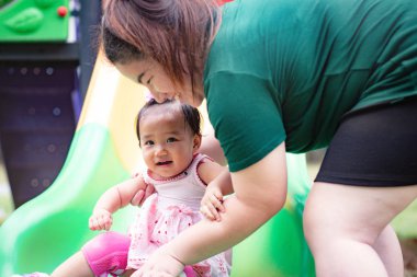 Anne ve kızı parkta sürgülü oynuyorlar.