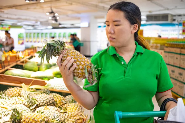 Kadın süpermarkette ananas seçiyor.