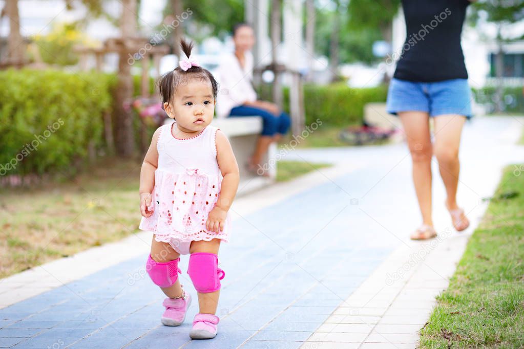 Little Asian adorable baby kid practicing walking on footpath in park, Baby girl with knee pads walking in park