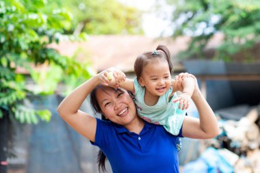 Asyalı anne bebeğini omuzlarında taşıyor.