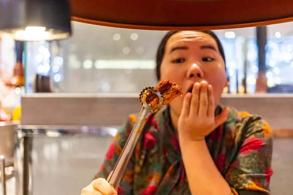 Woman using tongs to grip a piece of grilled meat in restaurant