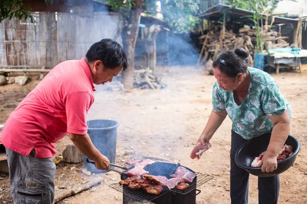 Asian couple grilling fresh meat over charcoal stove outdoor to preserve food