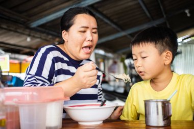 Asyalı anne oğlunu erişte dükkanında besliyor.