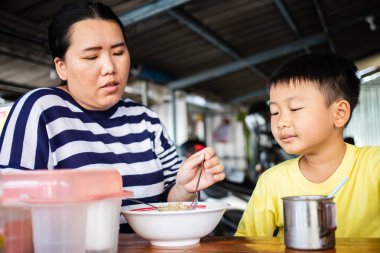 Asyalı anne oğlunu erişte dükkanında besliyor.