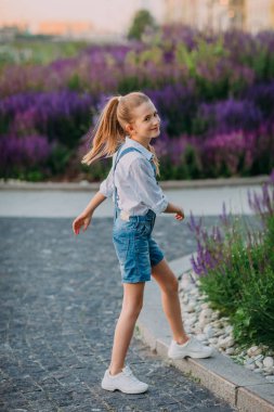 Beyaz gömlek ve kot kısa çiçek bahçesinde oynarken Gülümseyen güzel küçük kız