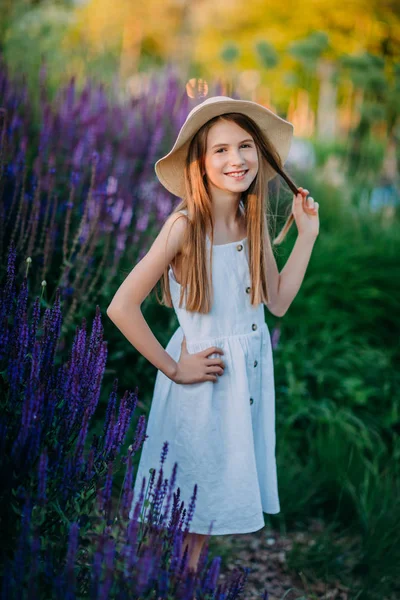 Gün batımında parkta beyaz elbise ve şapka ile gülümseyen küçük kız