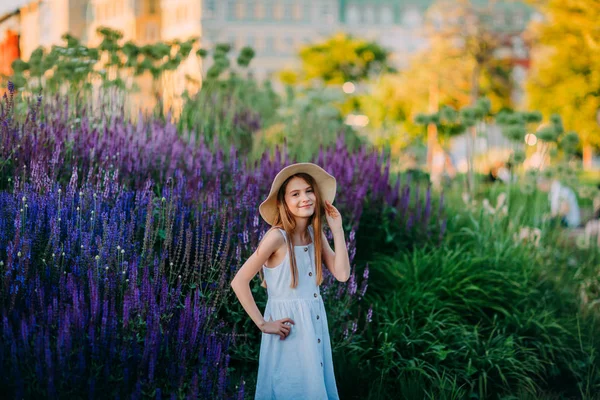 紫色の花の間の公園で白いドレスで微笑む小さな女の子 — ストック写真