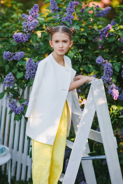 Zarif küçük kız, genç model leylak bahçesinde poz veriyor.