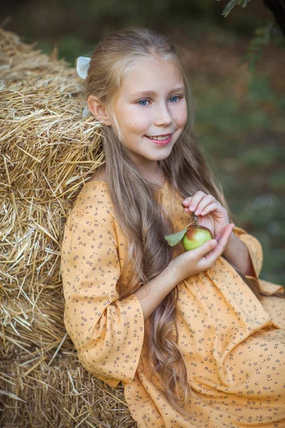 Mavi gözlü, sarı elbiseli uzun sarı saçlı güzel bir kızın portresi. Ellerinde nazikçe bir elma tutuyor.