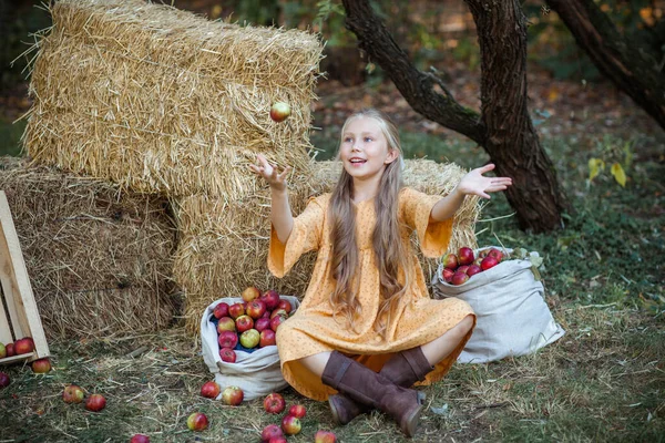 Sarı elbiseli mutlu kız sonbahar bahçesinde elmalarla oynuyor.
