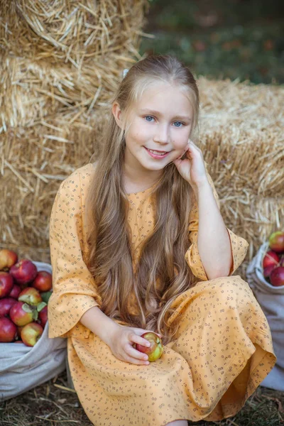 Mavi gözlü, uzun sarı saçlı, geçmişe dönük sarı elbiseli gülümseyen küçük bir kızın portresi. Dışarısı sakin ve kırsal.