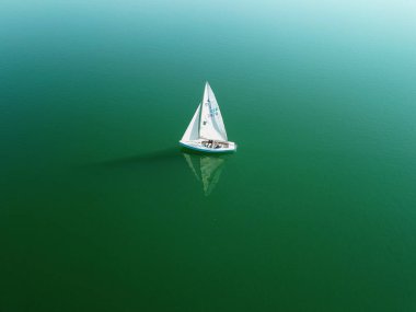 Alman volkanik gölü Maria Laach 'ta tek yelkenli. Beyaz yelkenli teknenin etrafında sadece yansıma ve yeşil görünen su..