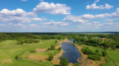 Nehir üzerinde uçan hava aracı videosu ve yaz gökyüzünde orman, tarlalar ve bulutlarla yeşil bir manzara.