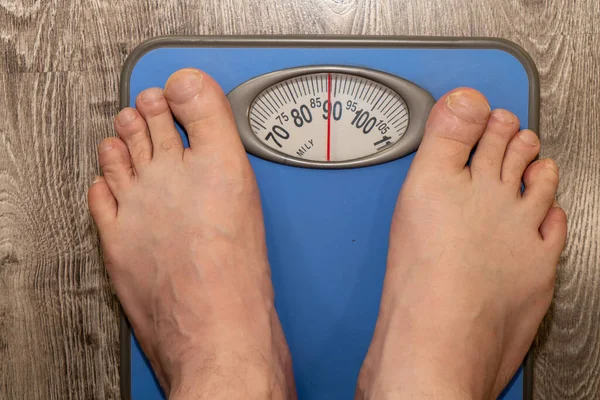 Man stands on weight scale, bare toes, overweight
