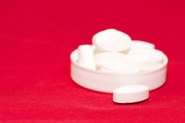 handful of white pills lies in the lid on a red