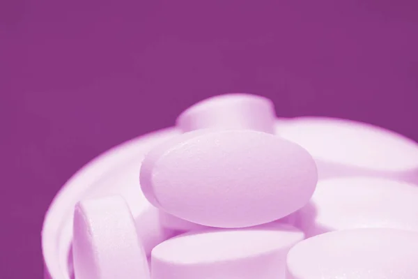 handful of white pills lies in the lid on a violet