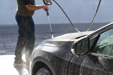 Adam oto yıkama servisini kullanıyor, araba kaputundaki araba şampuanlarını yıkıyor, siyah araba yıkama, basit iş, seçici odaklanma.