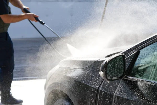 Adam oto yıkama servisini kullanıyor, araba kaputundaki araba şampuanlarını yıkıyor, siyah araba yıkama, basit iş, seçici odaklanma.