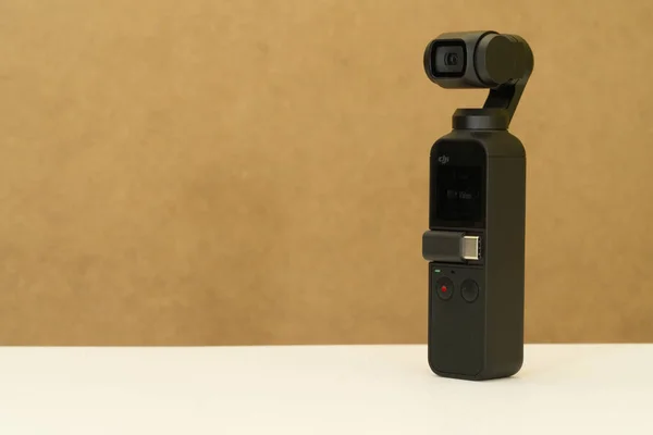 DJI osmo cep kamerası, cep büyüklüğünde video sabitleyici açık kahverengi arka planlı beyaz masada duruyor
